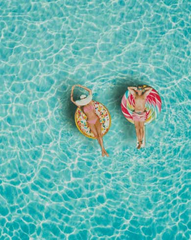 Two people relaxing on pool floats in clear blue water